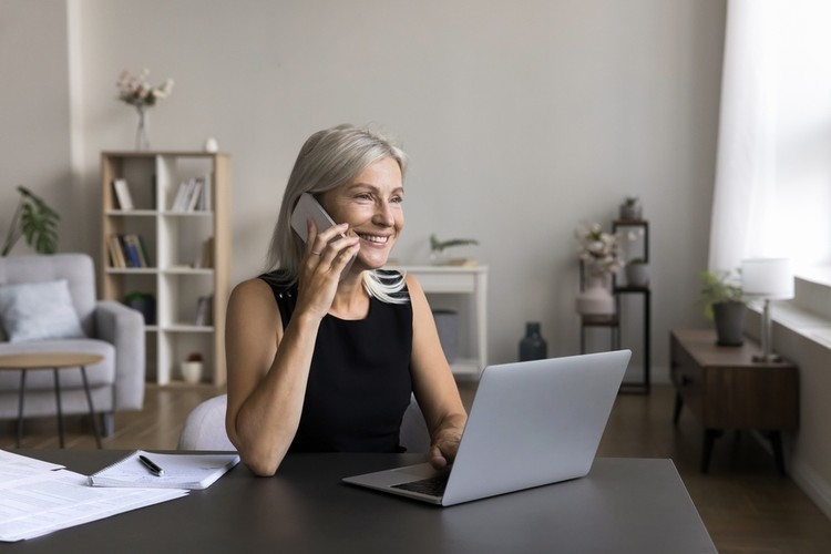 Smiling Woman Using Phone and Laptop at Desk